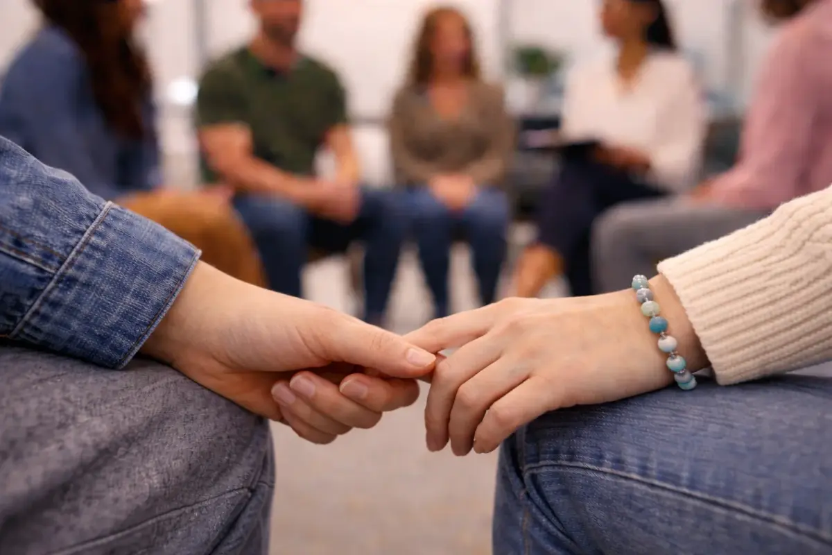 two hands holding each others whilst in an addiction recovery group session