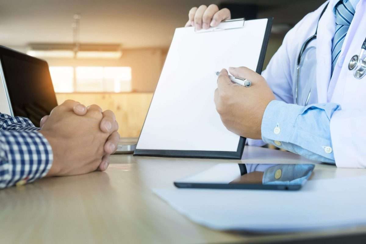 Patient listening intently to a doctor explaining patient symptoms or asking a question as they discuss paperwork together in a consultation