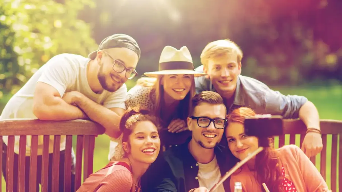 Group of friends posing in a park with a phone on a selfie stick to take a group photo