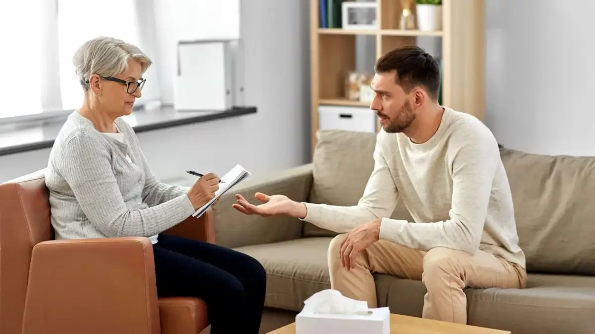 A psychologist explaining a concept to a patient sitting on a sofa during addiction treatment