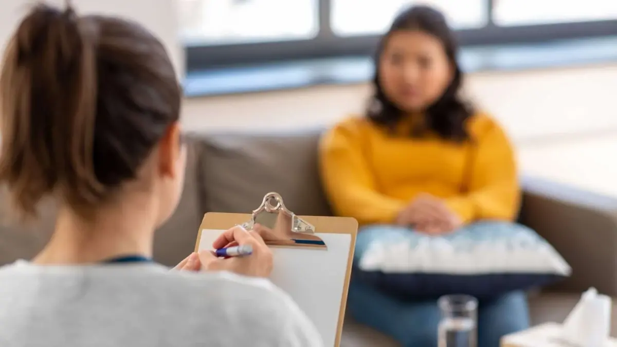 Therapist writing notes while a client talks