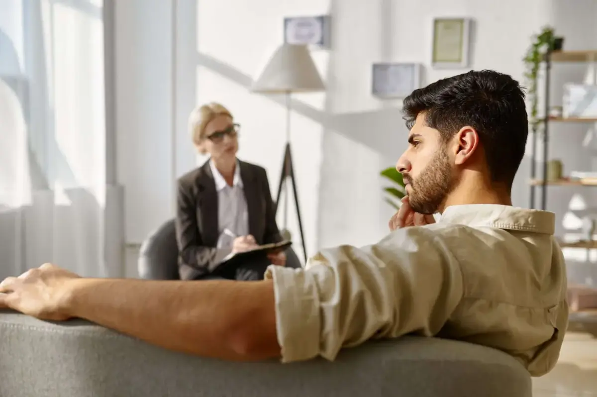 A man sitting on a couch talking to a psychiatrist for addiction