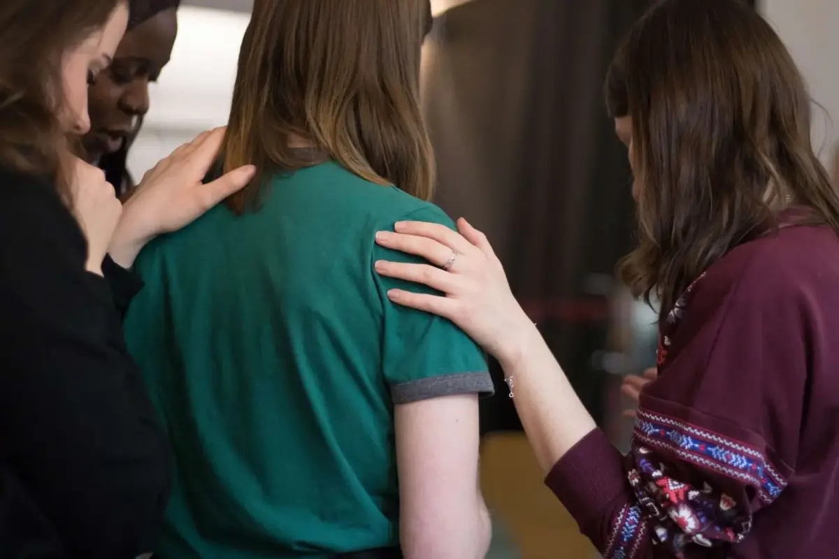 View of women putting a comforting hand on a woman's shoulder who is struggling with addiction
