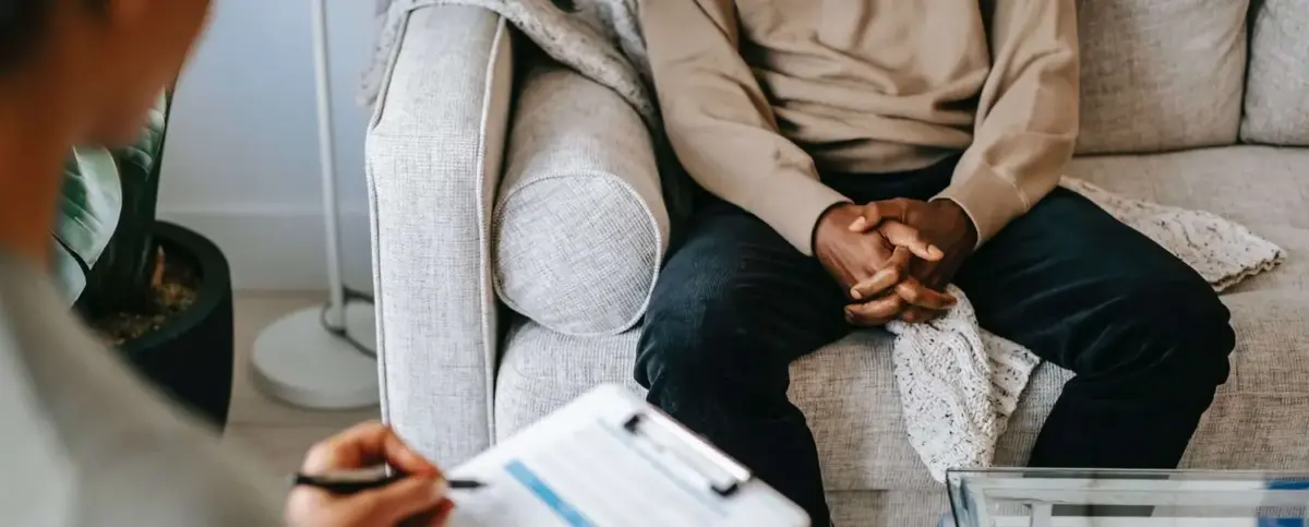Close up over shoulder photo of a man whose hands are clasped together during an addiction therapy session