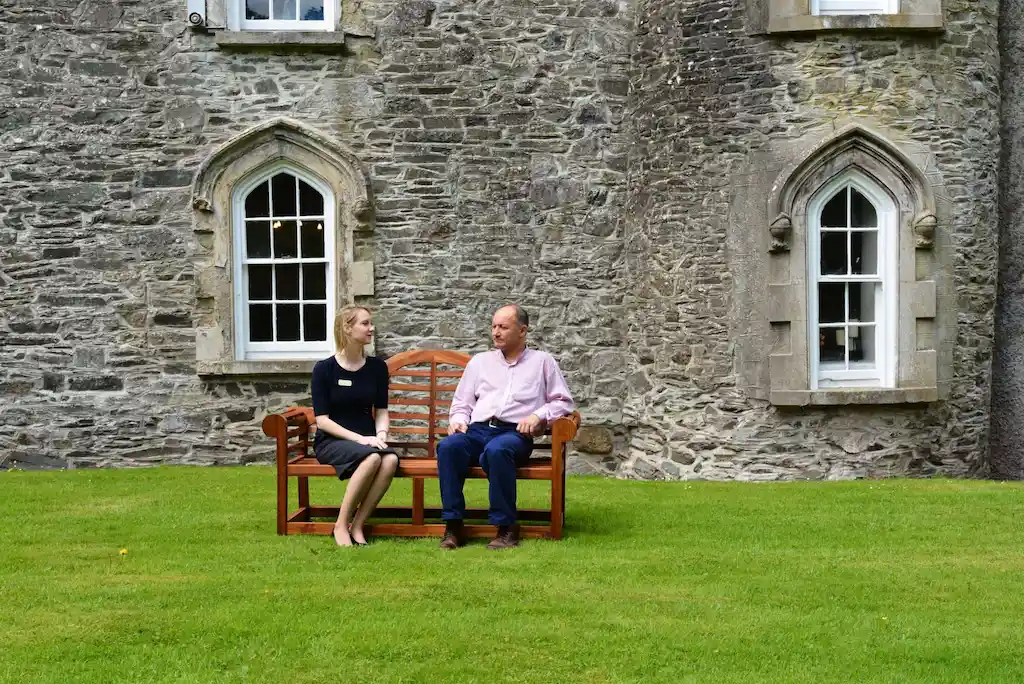 Outdoor therapy session at Smarmore Castle rehab for drug and alcohol addiction with a man and a therapist sitting on a bench outside the castle