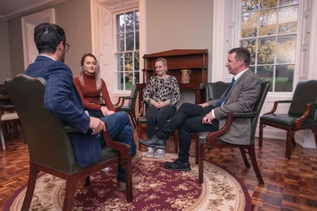 Four people (two women and two men) indoors sitting on chairs in a circle, talking about addiction recovery at Smarmore Castle