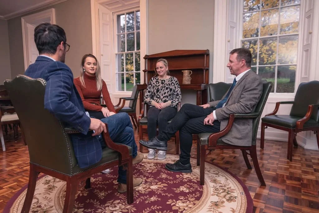 Four people (two women and two men) indoors sitting on chairs in a circle, talking about addiction recovery at Smarmore Castle