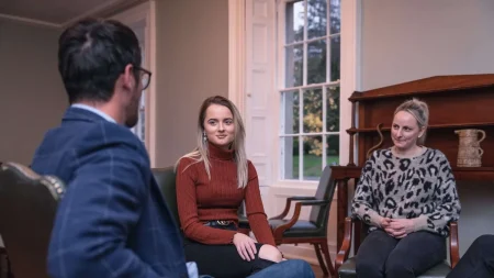 Three people inside sitting on chairs, talking, two women sitting across from a man