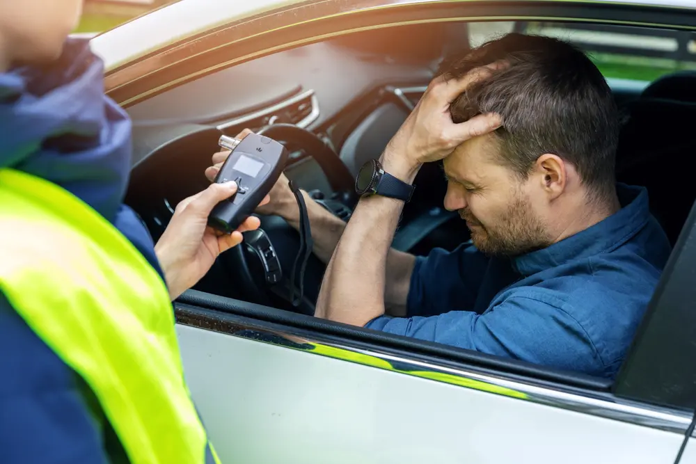 A man in the car holding his head after doing a breathalyser and learning about the dangers of drink driving.