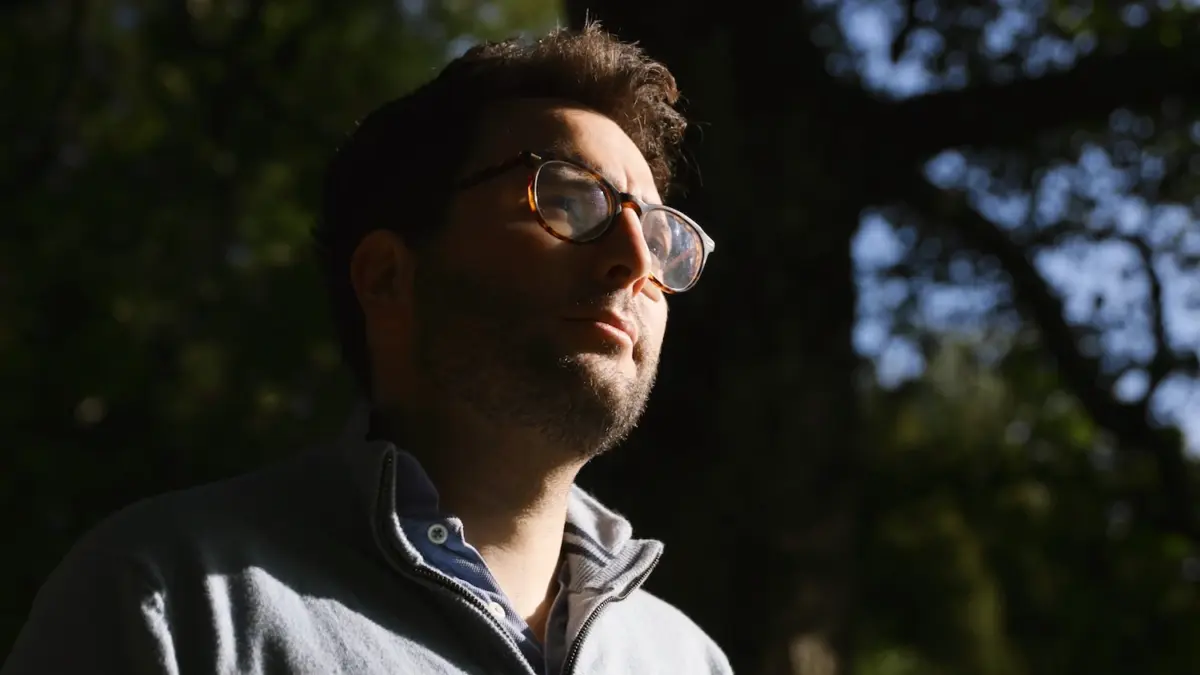 A man standing in the sunshine with half of his face in shadow looking pensive about addiction recovery