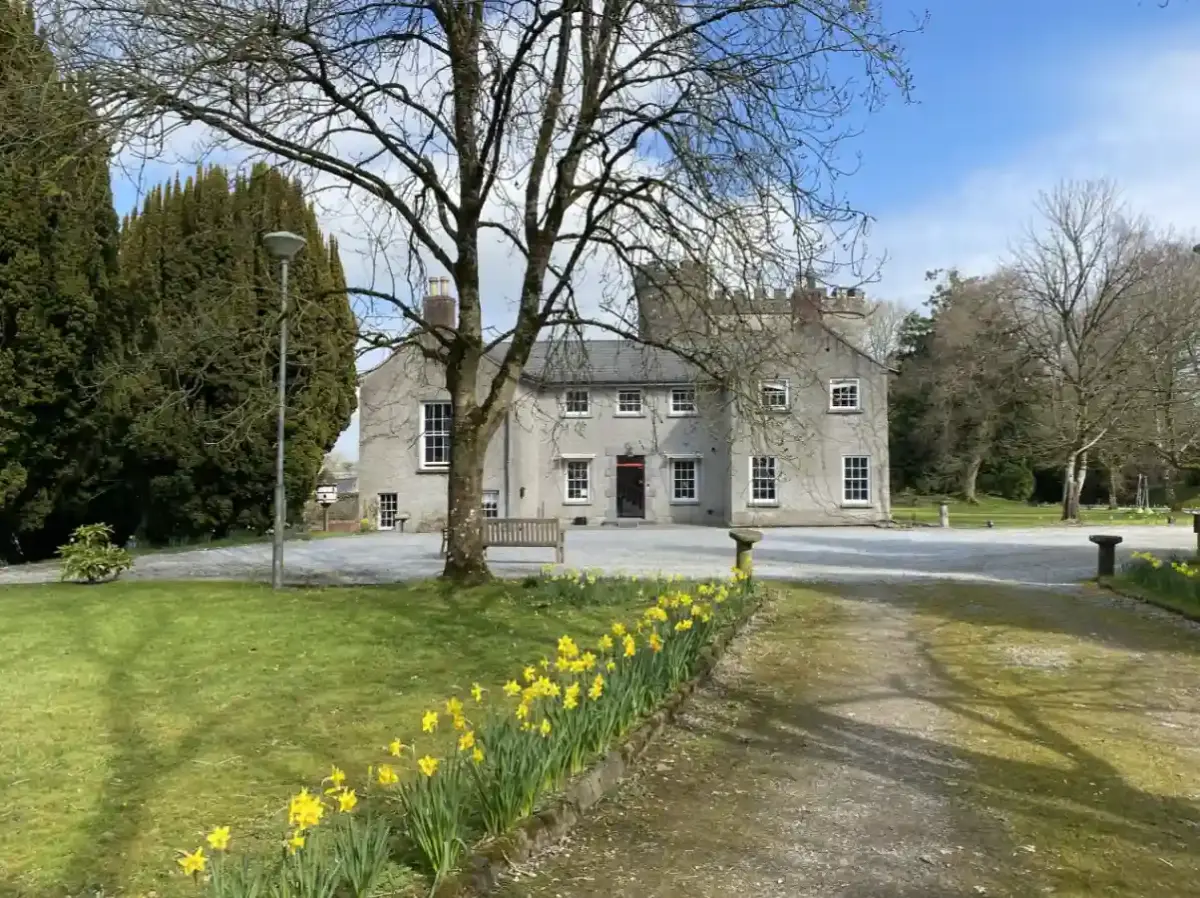Smarmore Castle from the rear, with trees, a lawn and daffodils - the place where patients can take part in gambling rehab.