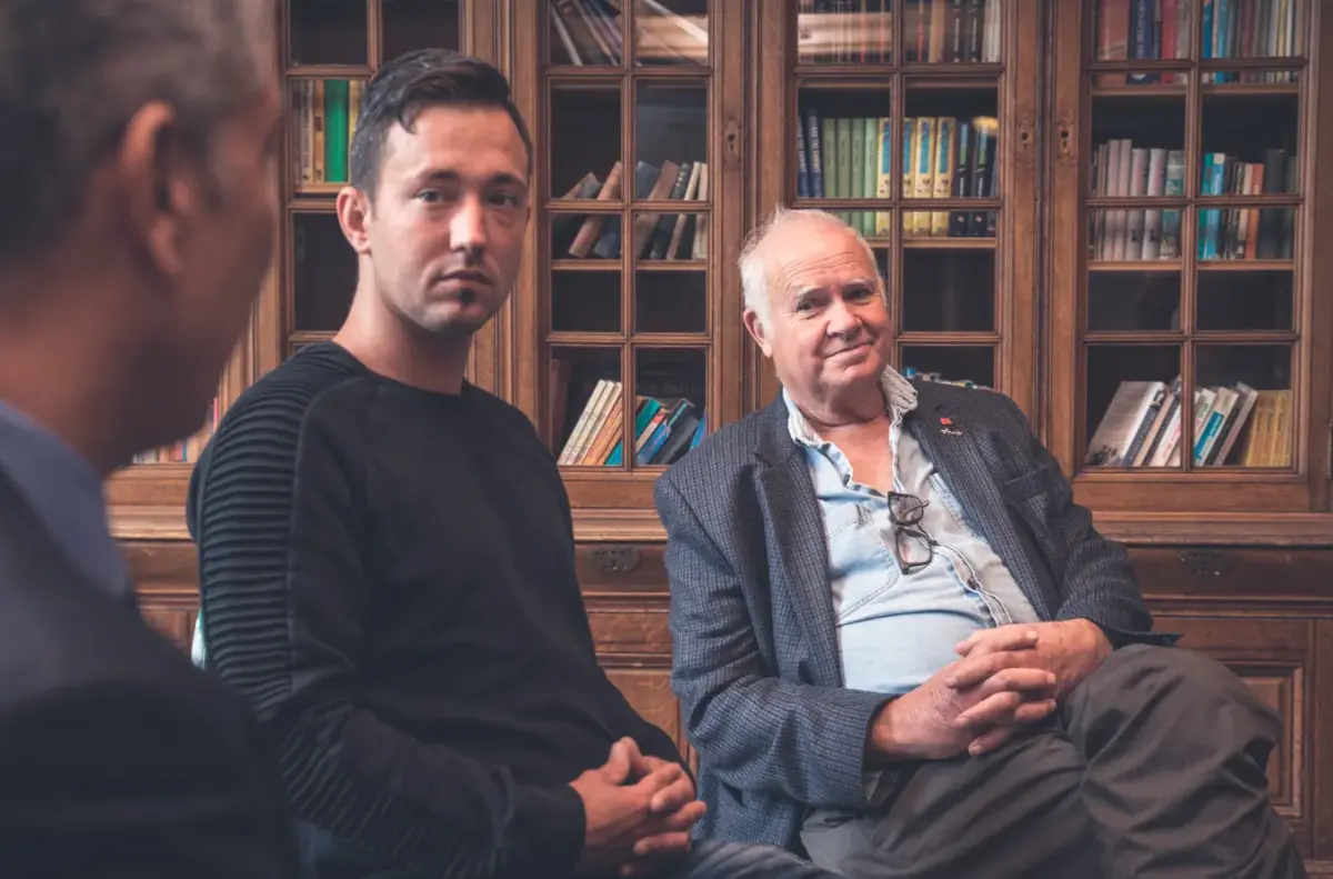 Three men discussing addiction rehab during therapy in a library.