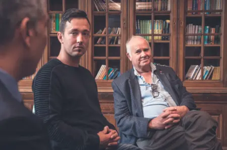 Three men discussing addiction rehab during therapy in a library.